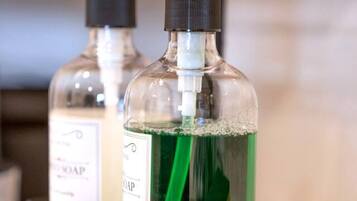 Two bottles of liquid soap in a metal rack with a green cleaning cloth.