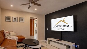 A modern living room with a sofa, a coffee table, a TV mounted on a black wall, and framed pictures on the wall. - 3BR Near West Point | Coffee Bar | Sleeps 6 (Highland Falls)