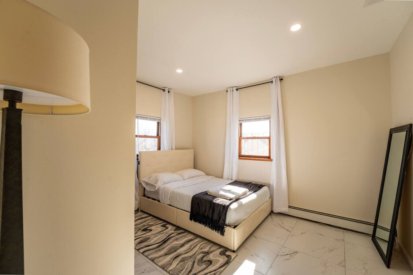 A bedroom with a bed, a window, a mirror, and a lamp.
