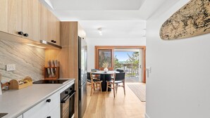 A modern kitchen with wooden cabinets, a built-in oven, and a dining area with a table and chairs. - Absolute Beachfront | Palm Cove Apt Sleeps 4 (Palm Cove)