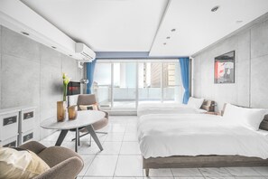 A hotel room with a bed, a desk, a chair, a small table, and a view of the city through large windows. - URBAN HOTEL 4480 (Sapporo)