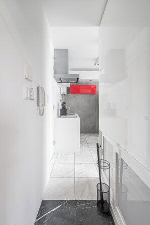 Een moderne keuken met witte kasten, een rode accentmuur en een marmeren vloer.