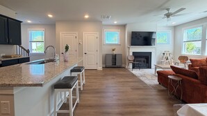 Una cocina moderna con una isla central, un área de estar con chimenea y un televisor montado encima.