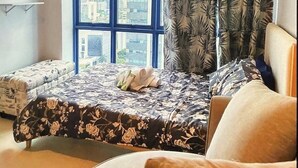 A bedroom with a large window, a bed with floral bedding, a chair, and a small table. - Luxury Studio in 38 Park Ave IT PARK (Lapu-Lapu)