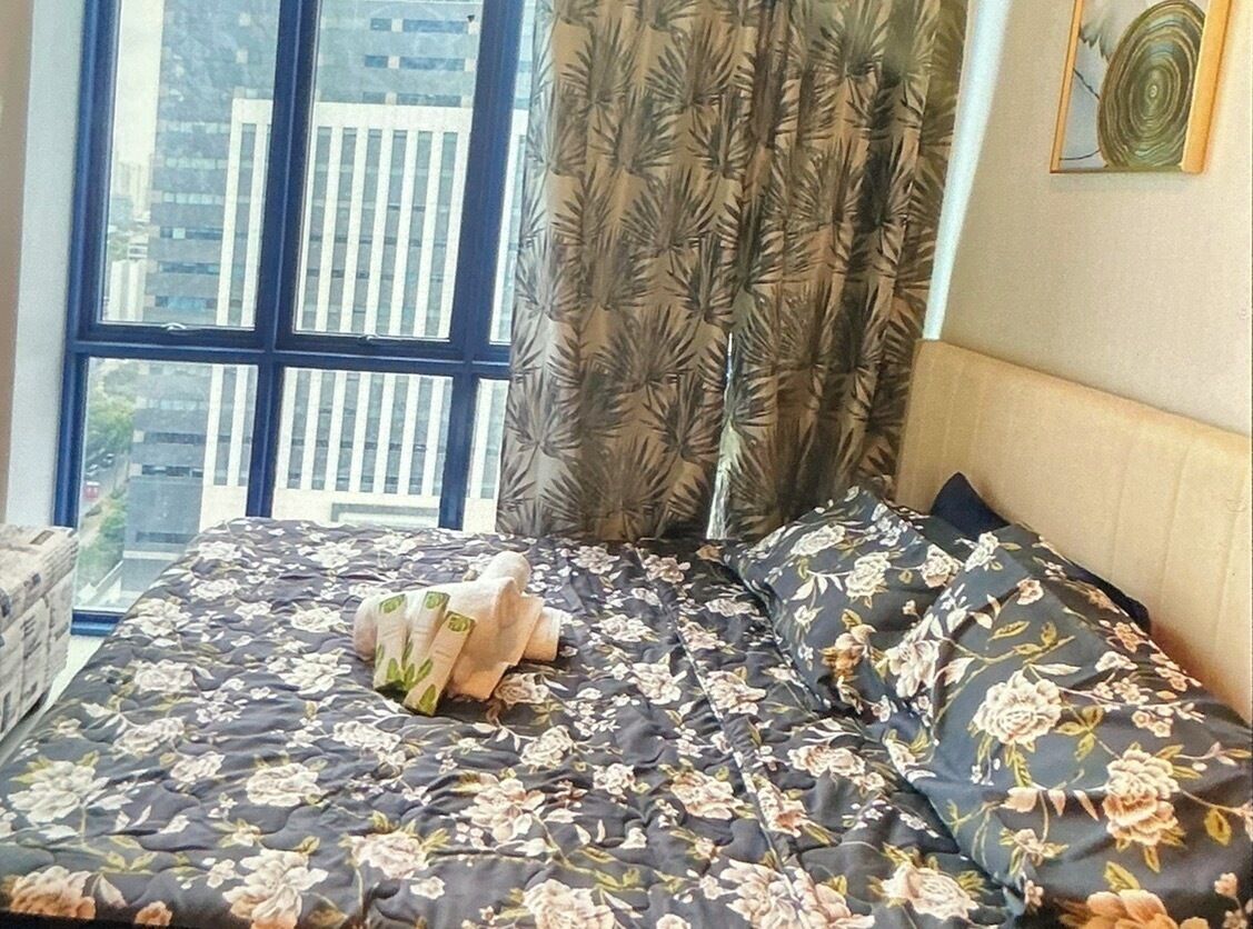 A bed with floral bedding, a window with a view of buildings, and a curtain with a leaf pattern.
