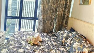 A bed with floral bedding, a window with a view of buildings, and a curtain with a leaf pattern.