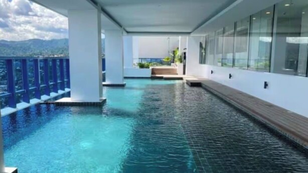 A swimming pool with clear water, surrounded by a wooden deck and glass walls, with a view of mountains in the background. - Luxury Studio in 38 Park Ave IT PARK (Lapu-Lapu)