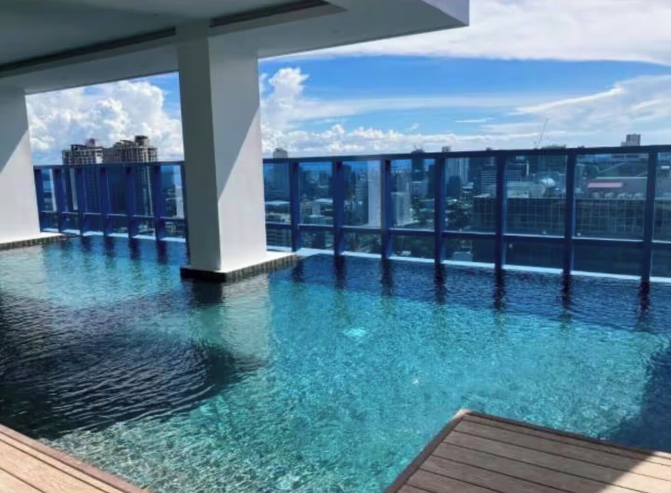 Una piscina infinita en la azotea con agua azul cristalina, rodeada por una barandilla de vidrio y vistas a un paisaje urbano.