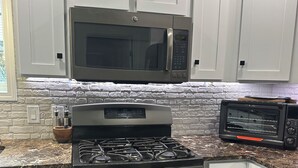 Una cocina con armarios blancos, una estufa de acero inoxidable, un microondas y un tostador.