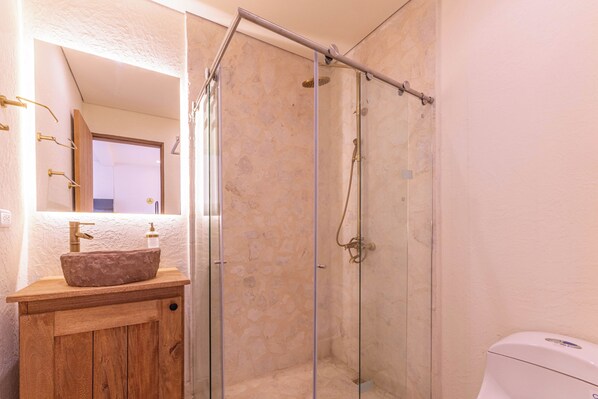 Een badkamer met een stenen wastafel, een glazen douchecabine en een wit toilet.