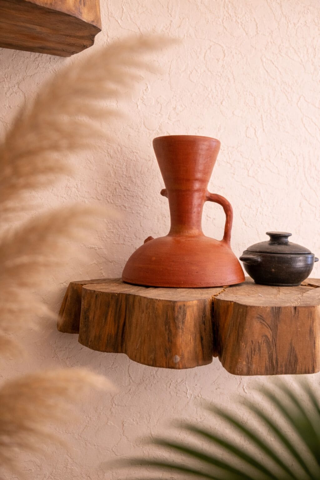 A rustic shelf with a clay pot and a black pot on a wooden base against a textured wall.