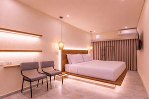 A hotel room with a bed, two chairs, a nightstand, a lamp, an air conditioning unit, and a window with curtains. - Casa Museo by HOUSY (Medellín)