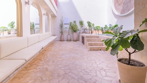 A sunlit courtyard with stone flooring, potted plants, and a seating area with cushions. - Casa Museo by HOUSY (Medellín)