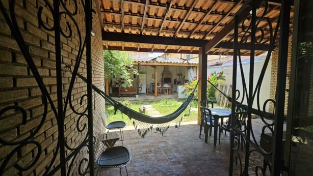 Une terrasse couverte avec un hamac, des sièges d’extérieur et une vue sur une maison dotée d’un mur en briques et d’un plafond en bois.