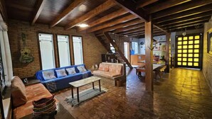 Un intérieur rustique avec des poutres apparentes, un mur en briques, un canapé bleu et un escalier menant à un deuxième étage.