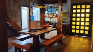Un intérieur rustique avec des murs en briques apparentes, des bancs en bois, une table en bois et un coin cuisine doté d’une grande fenêtre.