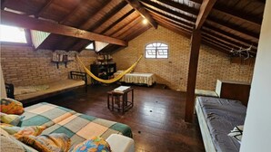 Une chambre mansardée au style rustique, avec des poutres apparentes, un hamac, un lit en mezzanine et un mur en briques.