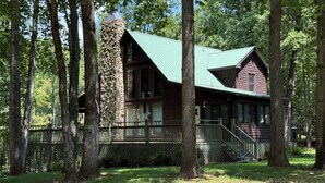 A cabin with a stone chimney, a green roof, and a wooden deck.