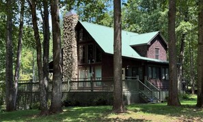 A cabin with a stone chimney, a green roof, and a wooden deck.
