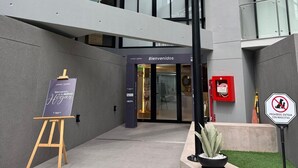 Ein mehrstöckiges Gebäude mit Glasfassade, einem 'Bienvenidos'-Schild, einem Verbotsschild für Haustiere und einer kleinen Staffelei mit einem Schild.