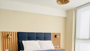 Ein modernes Schlafzimmer mit einem dunkelblauen Bett, einem Holz-Kopfteil, Nachttischen und einem großen Fenster.
