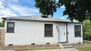 Une maison de plain-pied à l’extérieur blanc, avec une porte d’entrée, deux fenêtres avec volets, un petit porche et une boîte aux lettres.