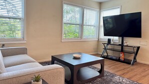 A living room with a sofa, a coffee table, a TV on a stand, and windows with blinds. - Historic Downtown Visalia 2BR • 1BA (Visalia)