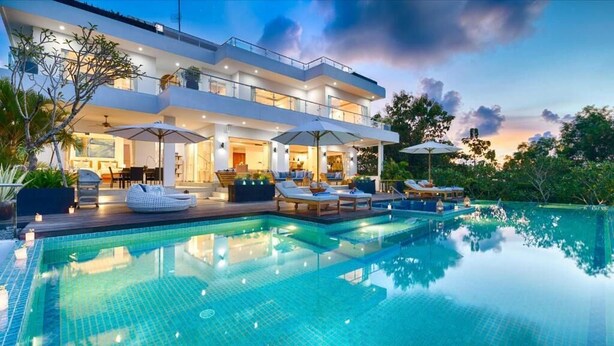 Et moderne hus med swimmingpool, udendørs møbler og en godt oplyst patio.