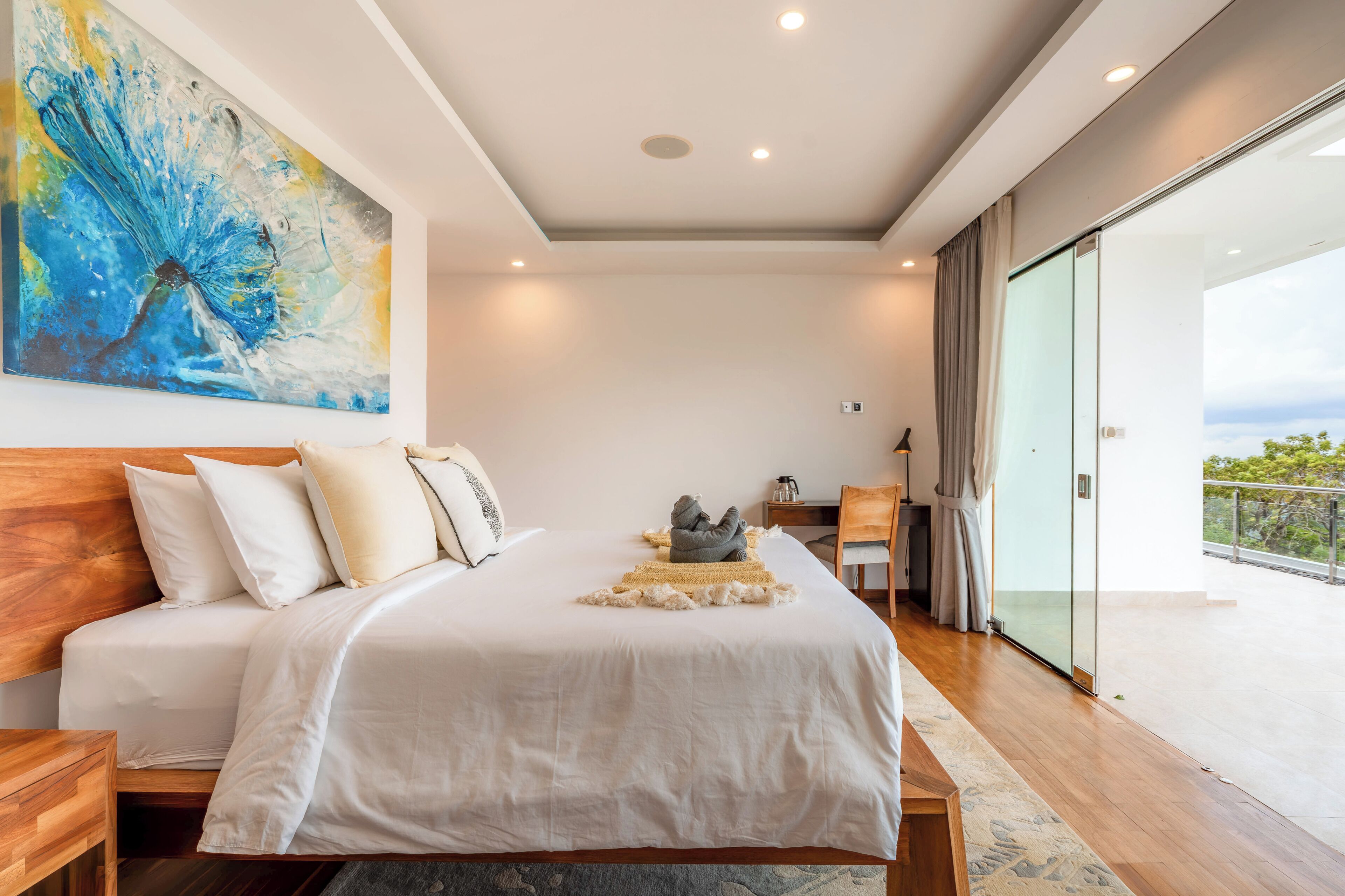 Een moderne slaapkamer met een groot bed, een schilderij, een bureau en een balkon met uitzicht.