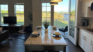 Eine Küche mit Granitarbeitsplatte, ein Essbereich mit Stühlen, ein Fernseher und Blick ins Freie.