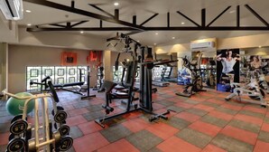 A gym with various exercise equipment, a large window, and a ceiling with exposed beams. - The Fern Residency Satara Maharashtra (Satara)