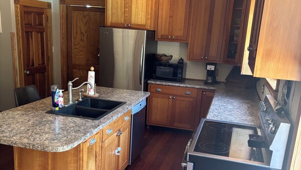 Una cucina con mobili in legno, un frigorifero in acciaio inox, un forno a microonde e un piano cottura.