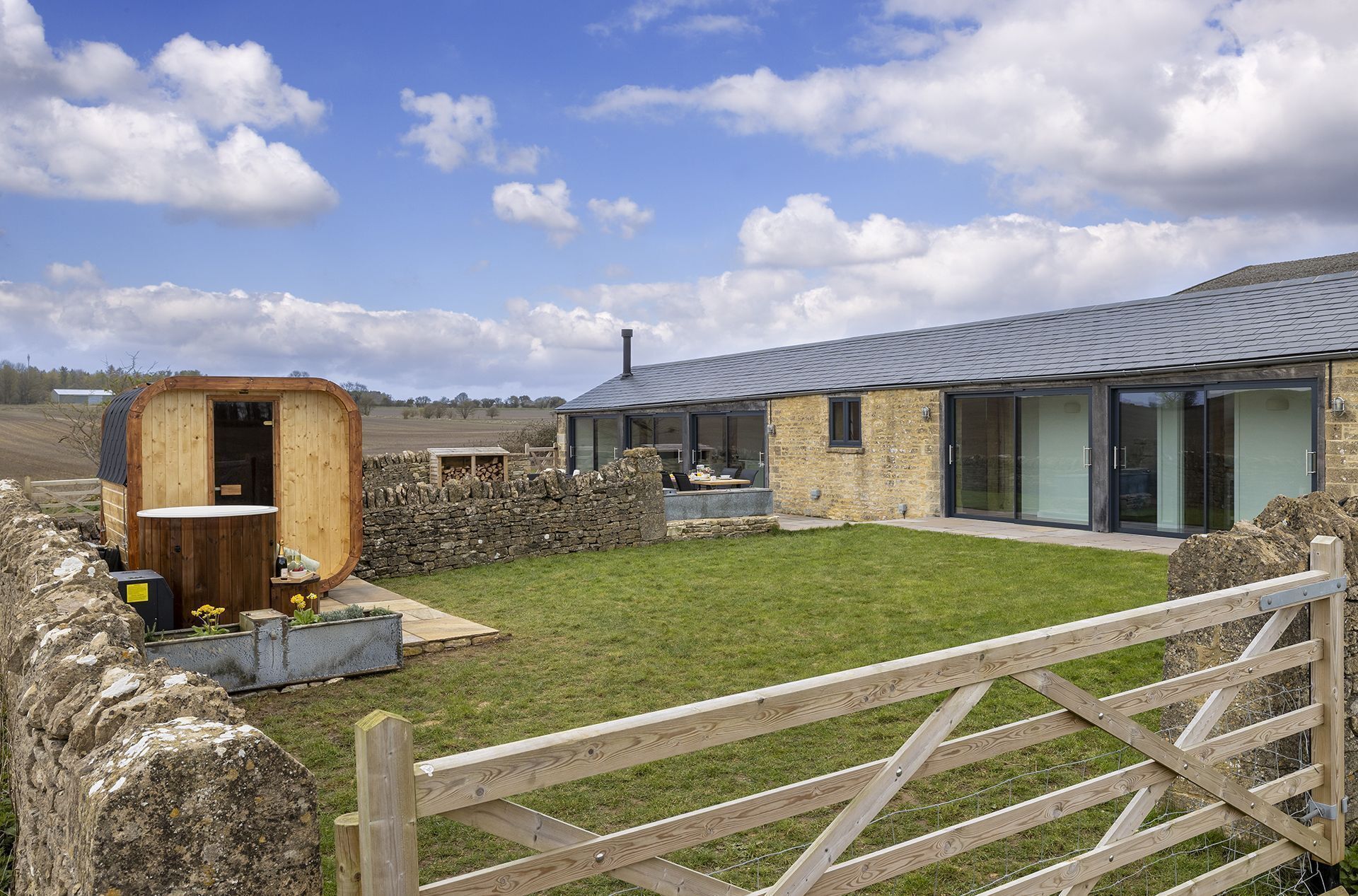 Una casa de campo moderna con un muro de piedra, una estructura de madera con un vano circular y un patio cubierto de césped.