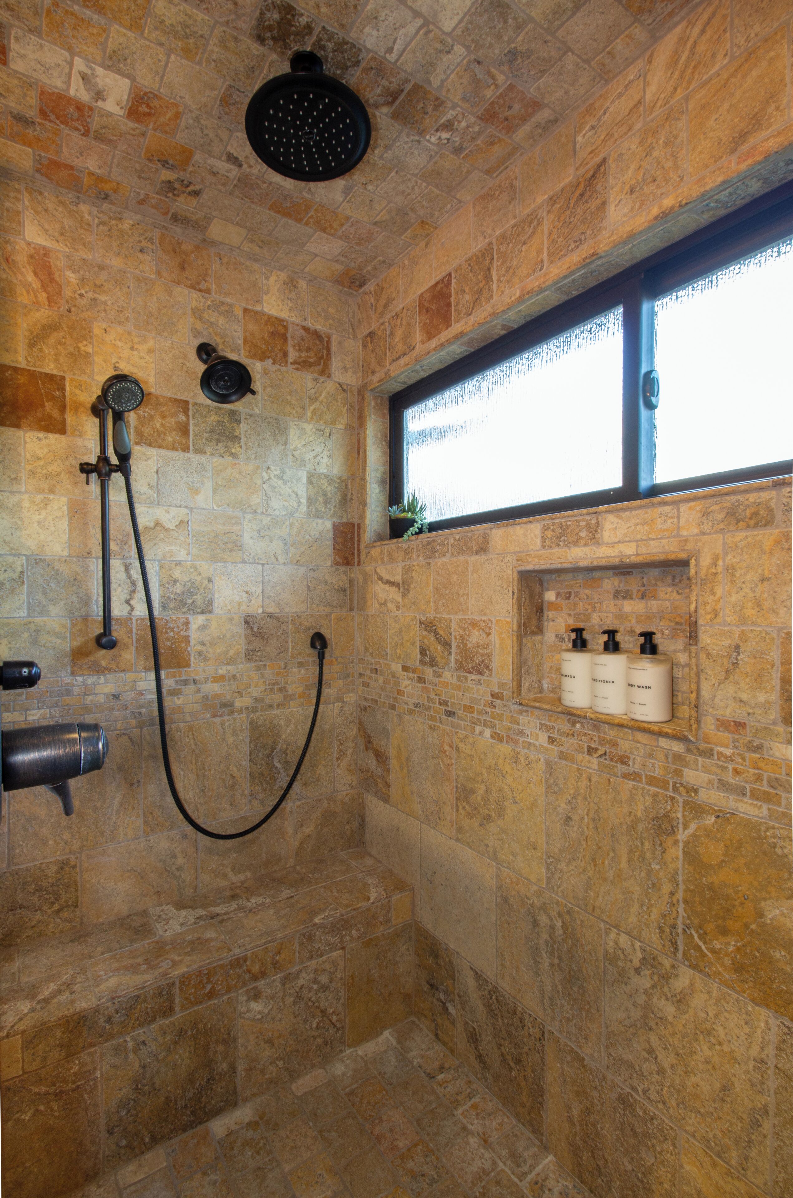 A stone-walled shower with a handheld showerhead and a wall-mounted faucet.