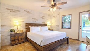 Ein Schlafzimmer mit einem hölzernen Bett, weißen Ziegelwänden, einem Deckenventilator und einem Fenster mit Blick.