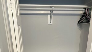 Un placard avec des portes blanches, un plancher en bois et une tringle à vêtements fixée à l’étagère supérieure.