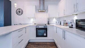 Una cucina moderna con pensili bianchi, una cappa aspirante in acciaio inossidabile, un forno integrato e un orologio a parete.