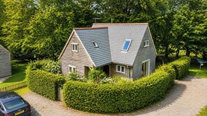 Een twee verdiepingen tellend huis met een schuin dak, omringd door goed onderhouden hagen en bomen.