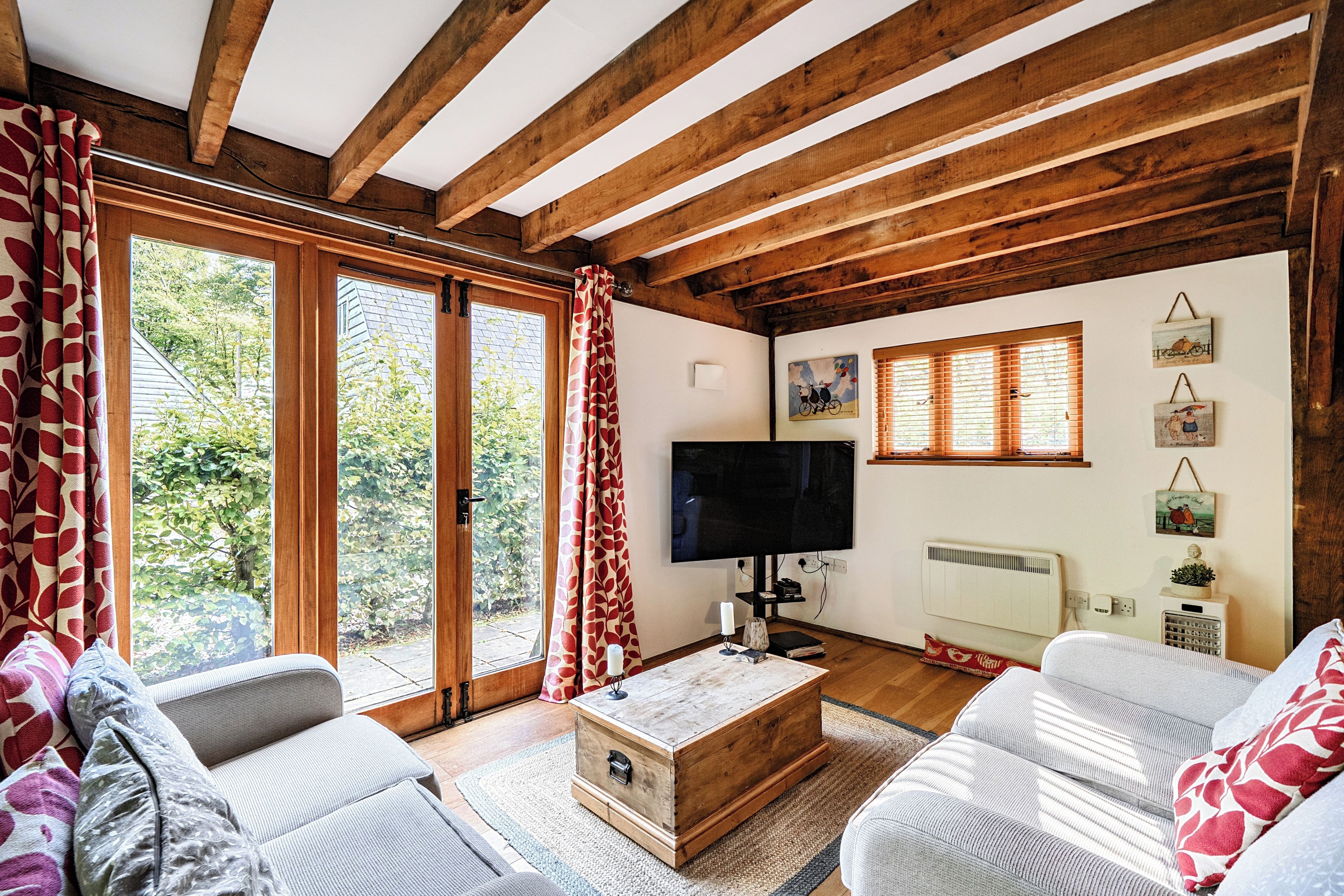 Uma sala de estar acolhedora com vigas de madeira, uma televisão grande e uma lareira.