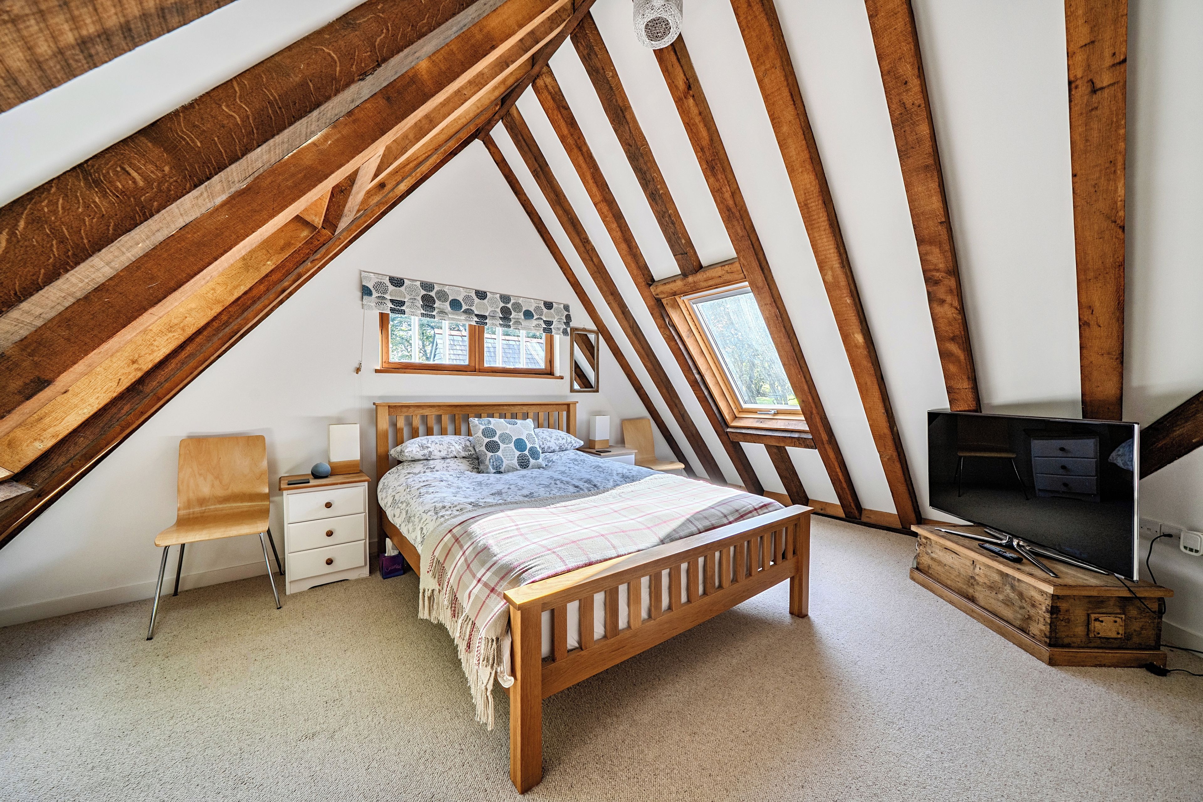 Un dormitorio con techo inclinado, una cama de madera, un televisor y una ventana.