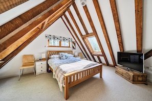 Une chambre avec un plafond en pente, un lit en bois, une télévision et une fenêtre.