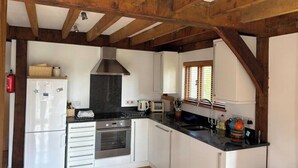 A kitchen with white cabinets, a stainless steel oven, a black range hood, and wooden beams on the ceiling.
