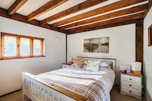 Une chambre avec un plafond en bois, un lit recouvert d’une courtepointe à carreaux, une table de chevet avec une lampe et un tableau accroché au mur.