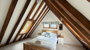 A bedroom with a sloped ceiling, a wooden bed, a nightstand, a dresser, and a window with a view.
