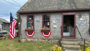 A building with a flag, two windows with flower boxes, and a sign that says 'OPEN'. - Historic Block Island Suite (New Shoreham)