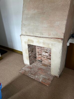 A fireplace with a brick interior and a concrete exterior, situated in a room with a carpeted floor.