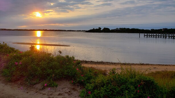 A calm lake at sunset with a dock extending into the water. - Historic Block Island Suite (New Shoreham)
