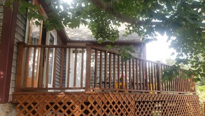 A wooden deck with a lattice railing, a white door, and a brick wall. - Historic Block Island Suite (New Shoreham)