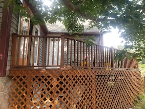 A wooden deck with a lattice railing, a white door, and a brick wall. - Historic Block Island Suite (New Shoreham)