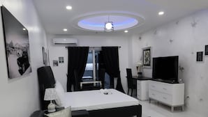 A modern hotel room with a bed, black and white furniture, a TV, and a ceiling light. - Kandy Haven - Studio Type Unit (Angeles City)